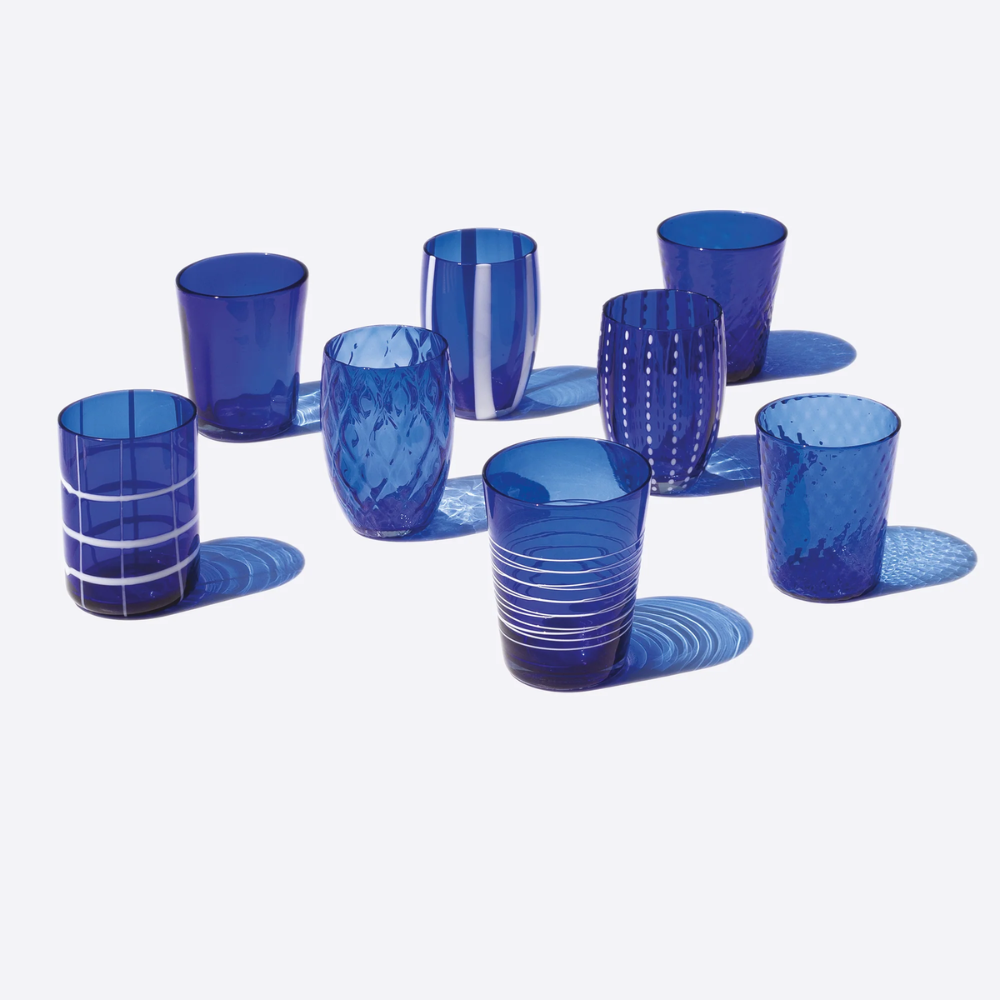 Set di otto bicchieri in vetro blu trasparente, ciascuno con disegni e texture diverse, su sfondo bianco.