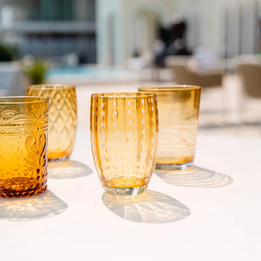 Vier amberkleurige glazen met diverse decoraties op een witte tafel buiten op een zonnige dag.