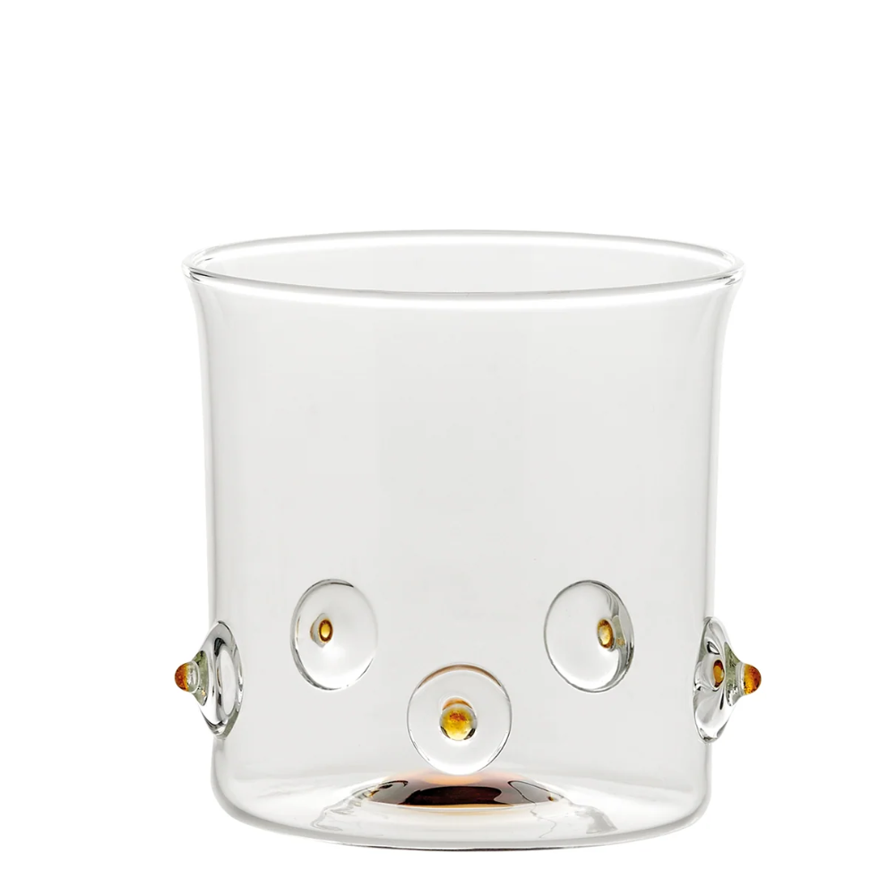 bicchiere di vetro trasparente con dettagli rotondi e piccoli elementi color ambra decorativi su sfondo bianco