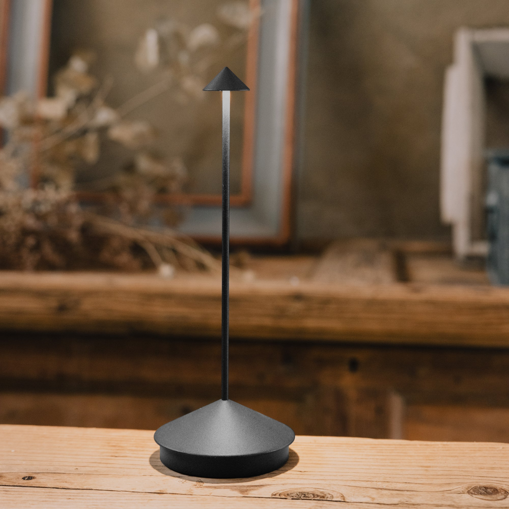 Oggetto per accendere candele in metallo nero opaco con base conica e asta sottile verticale, su tavolo di legno.