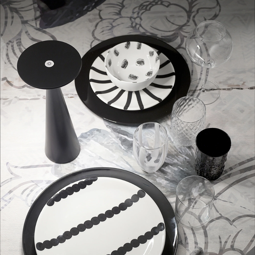 Weiße und schwarze Keramikteller und -schüssel mit Streifen- und Punktdetails, transparente und schwarze Glasbecher und ein Kerzenhalter