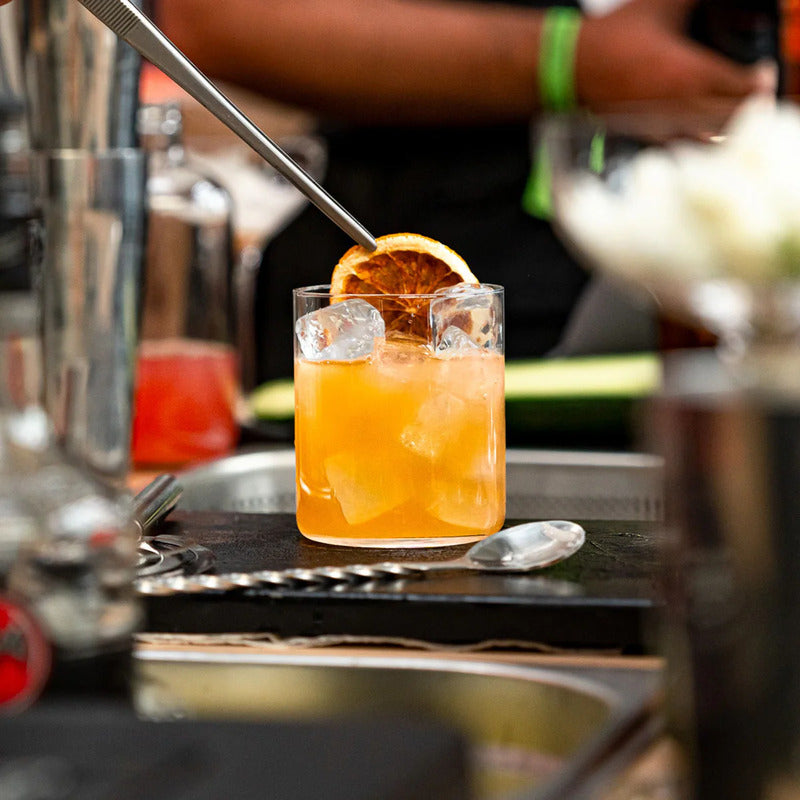 bicchiere trasparente con cocktail arancione, ghiaccio e fetta di agrume essiccato, ambientazione bar