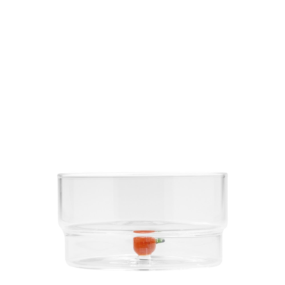 Jarrón transparente, forma circular, con una pequeña zanahoria naranja en el centro. Fondo blanco minimalista.