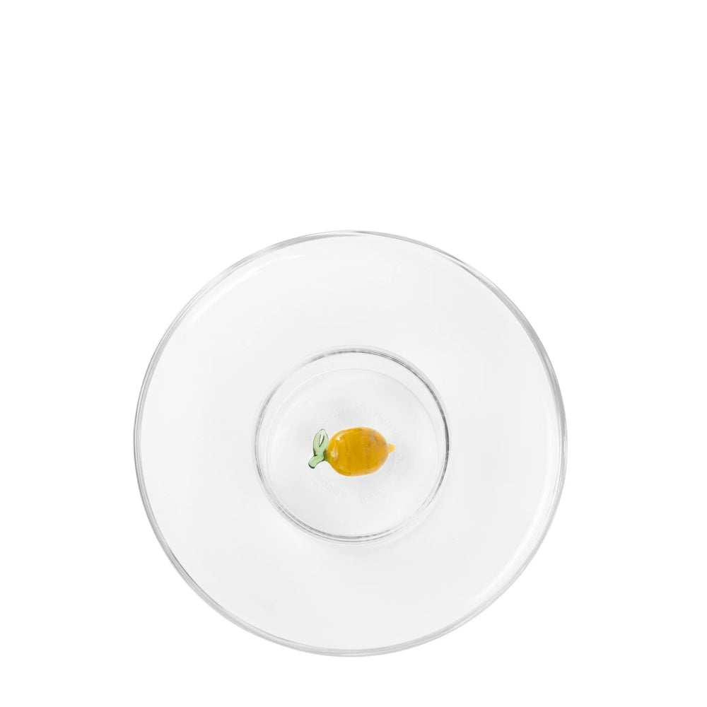 Piatto trasparente con un piccolo limone giallo al centro, decorato con una foglia verde. Ambientazione minimalista.