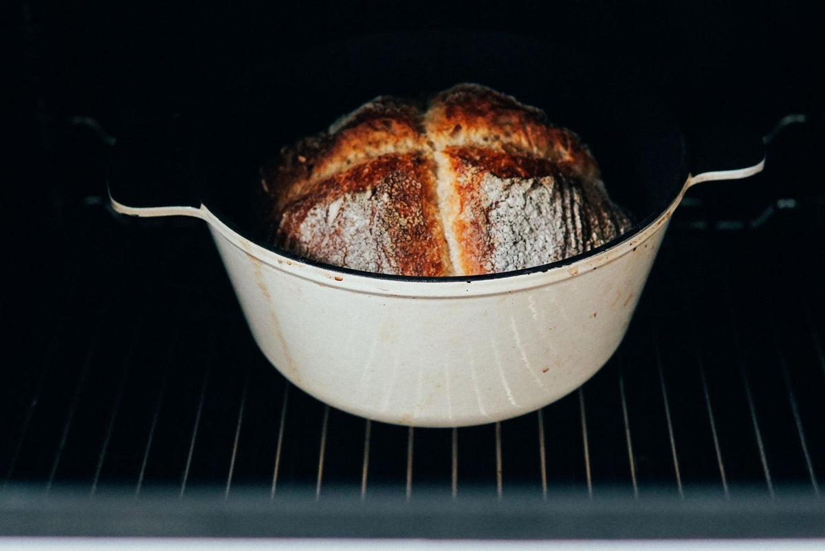 Pagnotta di pane dorato con crosta spessa in teglia bianca smaltata dentro forno acceso
