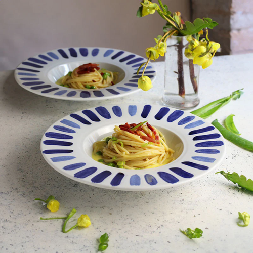 zwei weiße Teller mit blau bemaltem Rand mit Spaghetti, Erbsen und Kirschtomaten auf hellem Tisch mit Glasvase und
