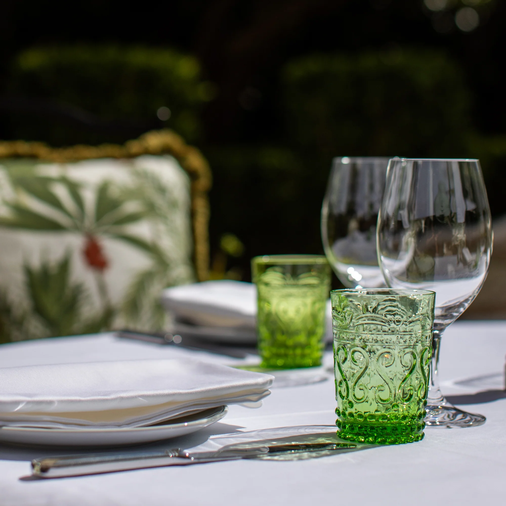 Groene glazen met reliëfdecoraties, transparante glazen, wit tafelkleed, bestek en kussen met botanisch patroon wazig