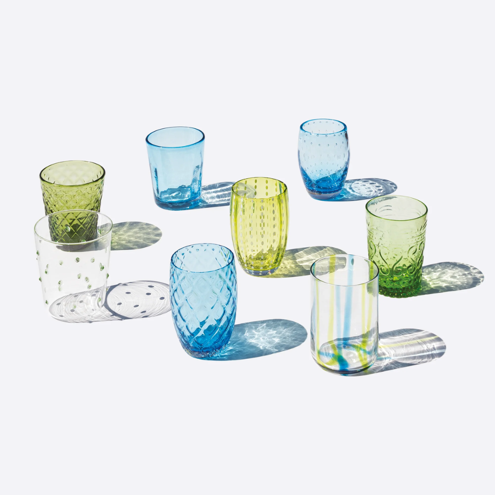 Set di otto bicchieri in vetro colorato trasparente con superfici bombate e decorazioni a rilievo, su sfondo bianco.