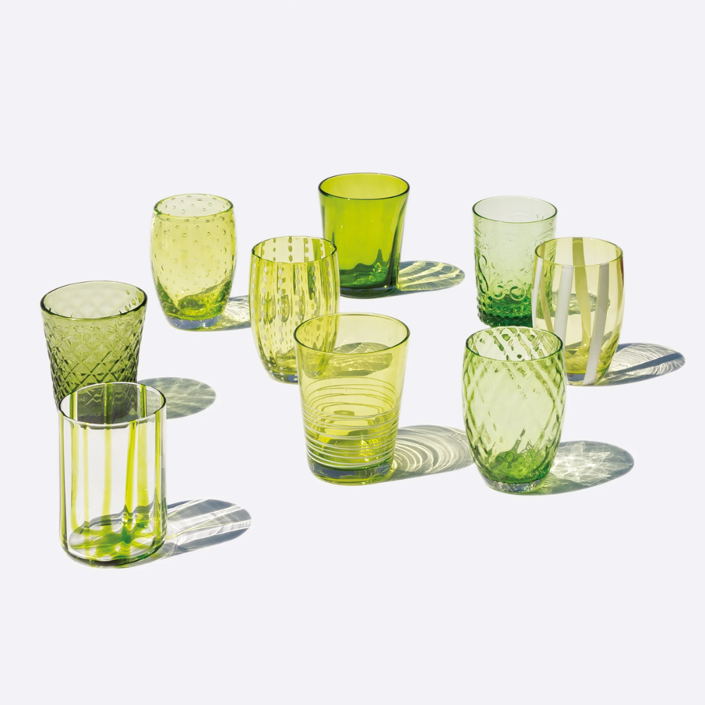 Nove bicchieri in vetro verde trasparente con diverse texture e motivi, su sfondo bianco luminoso.