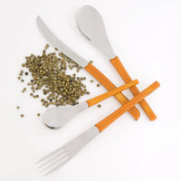 Cuchillo, cuchara, tenedor y cucharilla con mangos naranjas translúcidos y pimienta verde esparcida sobre fondo