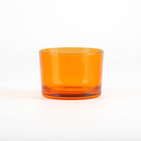 Bicchiere di vetro trasparente arancione con base spessa, posizionato su sfondo bianco.