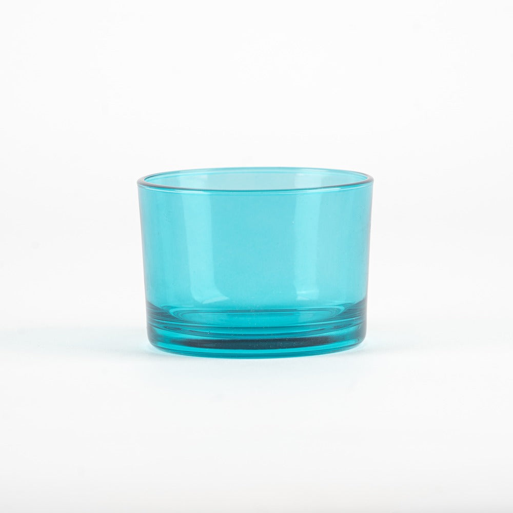 Bicchiere di vetro trasparente di colore azzurro, con base liscia e bordi arrotondati, su sfondo bianco.