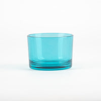 Bicchiere di vetro trasparente di colore azzurro, con base liscia e bordi arrotondati, su sfondo bianco.