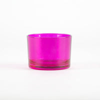 Bicchiere di vetro trasparente di colore fucsia, con base liscia e forma cilindrica, su sfondo bianco.