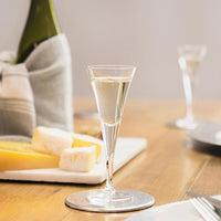 vaso de vidrio transparentee csobre clear liquid, cheeses sobre board y bottiglia verde csobre tovagliolo, sobre mesa de madera