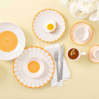 Set de table avec assiettes blanches et orange, couverts gris, une tasse de thé et une assiette avec un œuf au plat sur fond jaune.