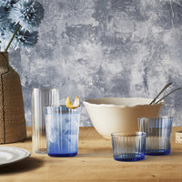 Transparante blauwe glazen met strepen, golvende witte kom, vazen met lichtblauwe bloemen en tafel van