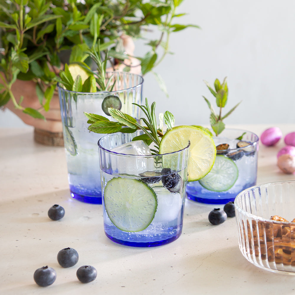 Drie transparante glazen met blauwe basis met drank met ijs, limoenplakjes en komkommer