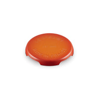 Coperchio di ceramica arancione brillante, rotondo, con scritte in rilievo: "LE CREUSET EST 1925 MADE IN FRANCE".