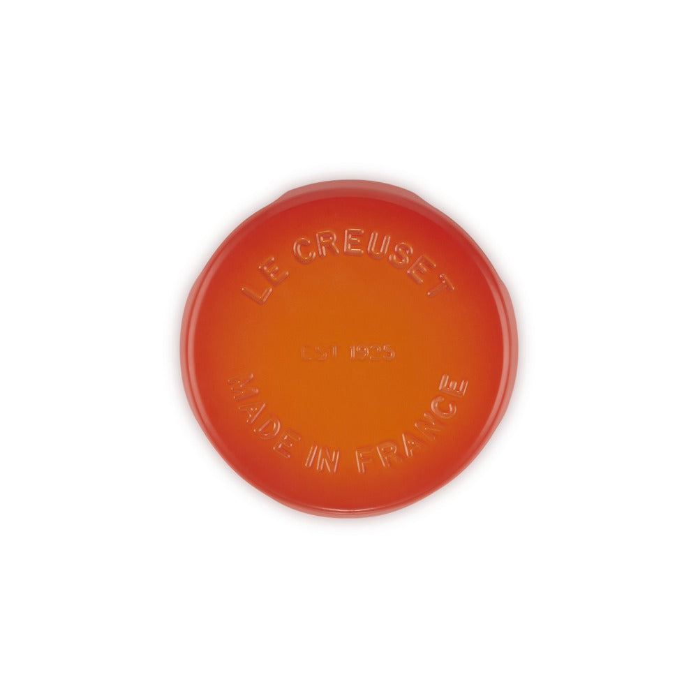 Disco di ceramica rotondo arancione con logo "LE CREUSET" e "MADE IN FRANCE" in rilievo. Fondo liscio, superficie lucida.