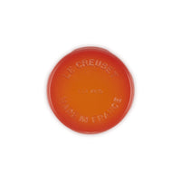 Disco di ceramica rotondo arancione con logo "LE CREUSET" e "MADE IN FRANCE" in rilievo. Fondo liscio, superficie lucida.