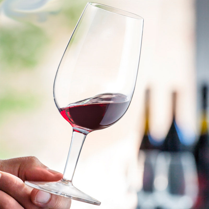 Transparentes Glas-Weinglas mit blassrotem eingegossenem Wein, in der Hand gehalten, unscharfe Flaschen im Hintergrund