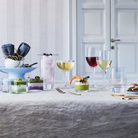 Gedekte tafel met glazen, kleurrijke cocktails en kleine desserts in transparante bakjes, op licht tafelkleed.