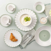 Tafelset met witte borden, kopjes en kommen met groene rand en bloemendecoratie, croissant, yoghurt met avocado en koffie.