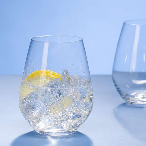 Calice di vetro con ghiaccio e fetta di limone, su sfondo blu. Un altro calice vuoto è parzialmente visibile dietro.