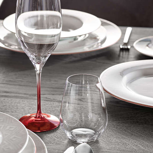 Set aus Tellern und Gläsern auf Holztisch. Hohes Glas mit rotem Fuß und kurzes transparentes Glas. Edelstahlbesteck.