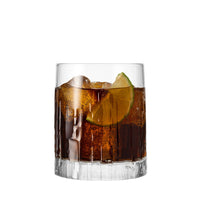 Dark cocktail in a clear glass with ice and a lime slice. Darkened background and striped texture.