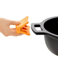 Ein orangefarbener Silikonhandschuh wird von einer Hand neben einem schwarzen Topf mit Griffen gehalten.