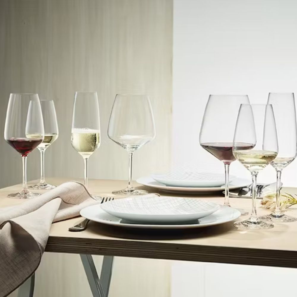 Gedeckter Tisch mit zwei weißen Tellern, beiger Serviette und sechs transparenten Gläsern mit Rot-, Weiß- und Schaumwein, Hintergrund