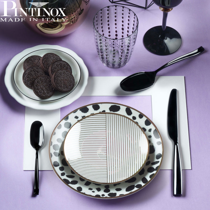 Set tavola con piatti decorati a pois e linee dorate, posate nere lucide, bicchiere trasparente a pois