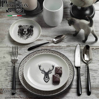 Elegante Teller mit Tierdekorationen, Stahlbesteck und Keramikkatze, auf Holztisch.