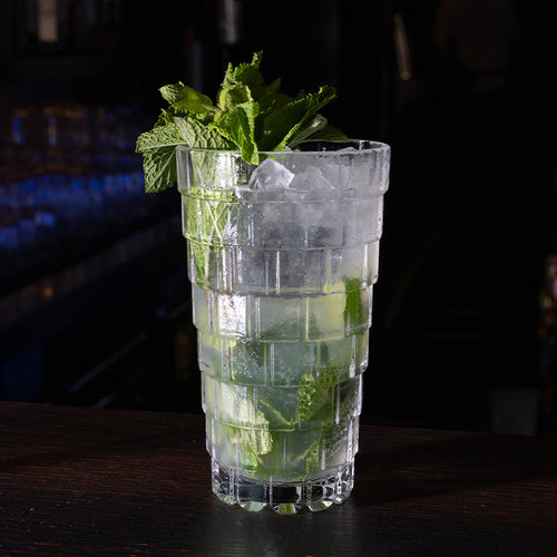 Transparenter Glasbecher mit Eisd drink, mint leaves und Eis, auf dark surface in dimly lit setting.