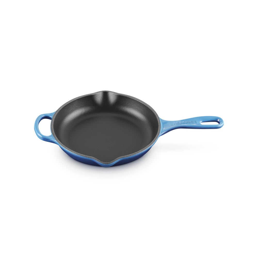 Poêle en fonte émaillée, couleur bleue, forme ronde avec manche et bord ondulé, surface intérieure noire.