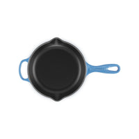 Poêle en fonte avec manche bleu, surface intérieure noire et lisse, forme ronde, sur fond blanc.