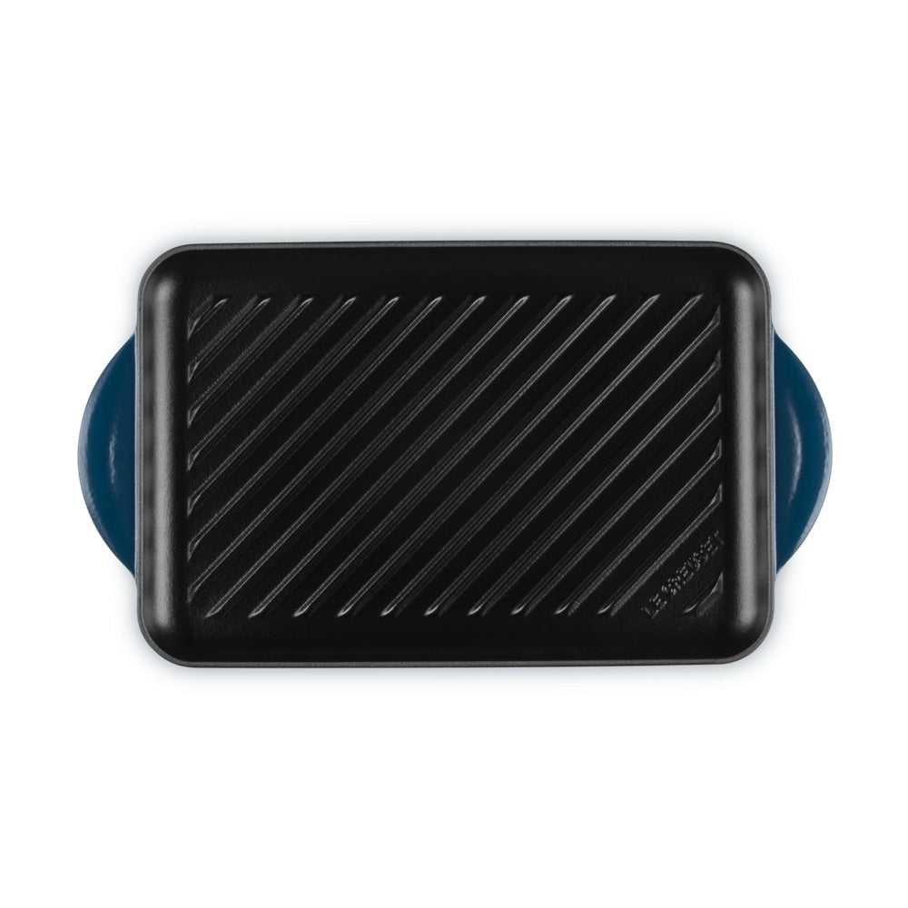 Piastra rettangolare nera con scanalature, manici blu; superficie liscia, adatta per cucinare su fornello o griglia.