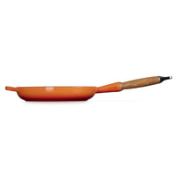 Poêle de couleur orange avec manche en bois, posée sur fond blanc, sans autres éléments visibles.
