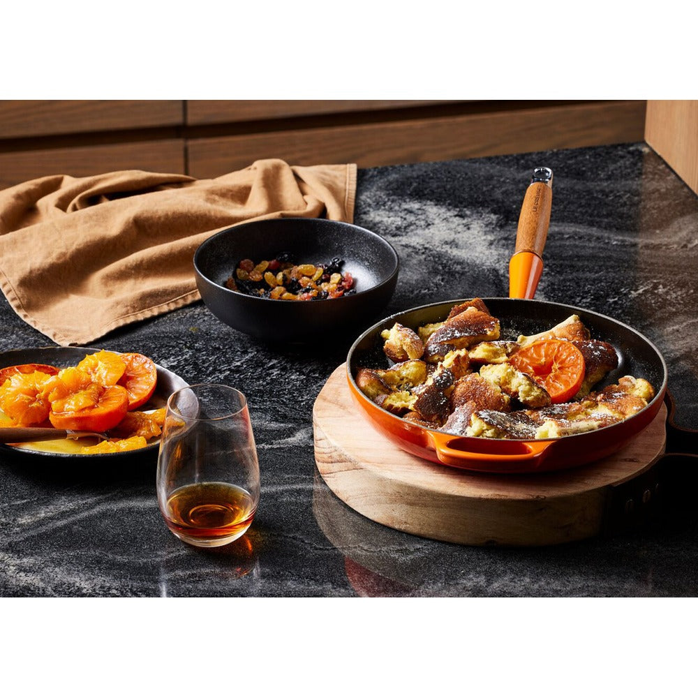 Bol noir avec fruits secs, plat orange avec dessert, tranches d'orange sur assiette sombre, verre de liqueur sur surface sombre.