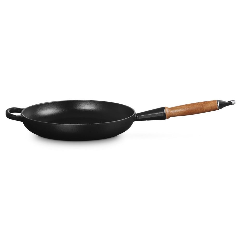 Zwarte gietijzeren koekenpan met houten handgreep, ronde vorm en platte bodem, op witte achtergrond.