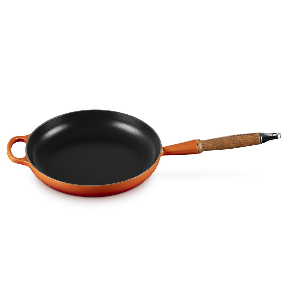 Ronde koekenpan met mat zwarte bodem en oranje rand, houten handgreep. Gladde bodem zonder zichtbare inhoud.