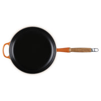 Zwarte ronde koekenpan met oranje handgreep, van vermoedelijk metaal en hout.