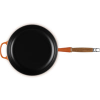 Padella nera con manico arancione e legno, superficie brillante, vista dall'alto.