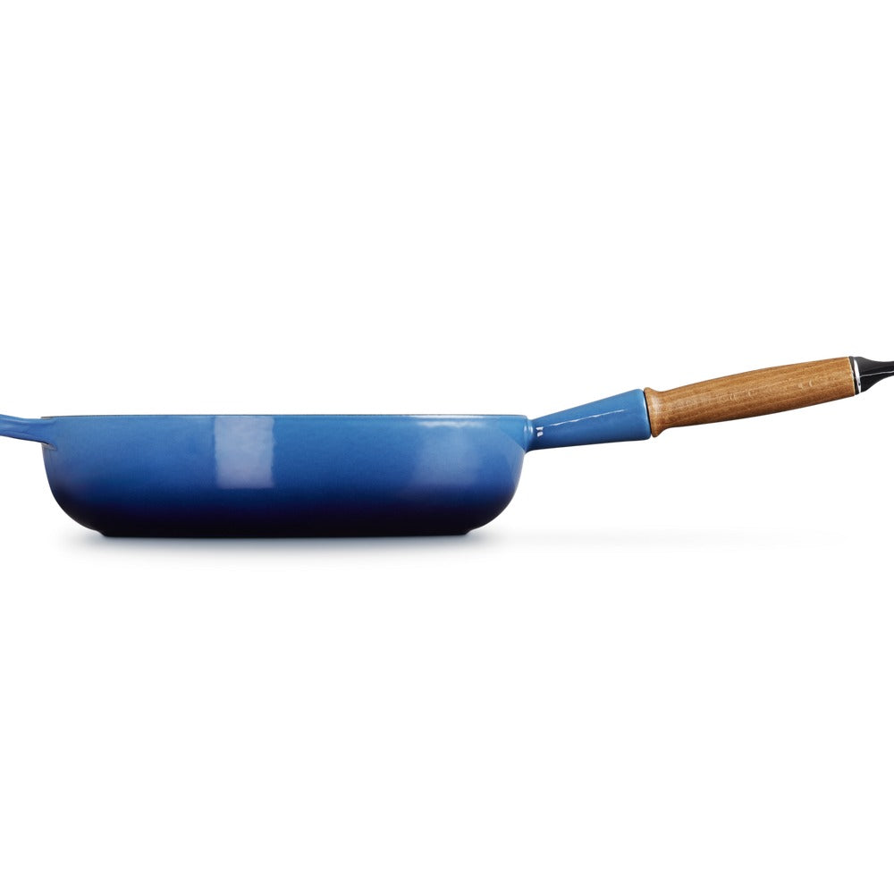 Padella blu con manico in legno, forma rotonda e base piatta, su sfondo bianco.
