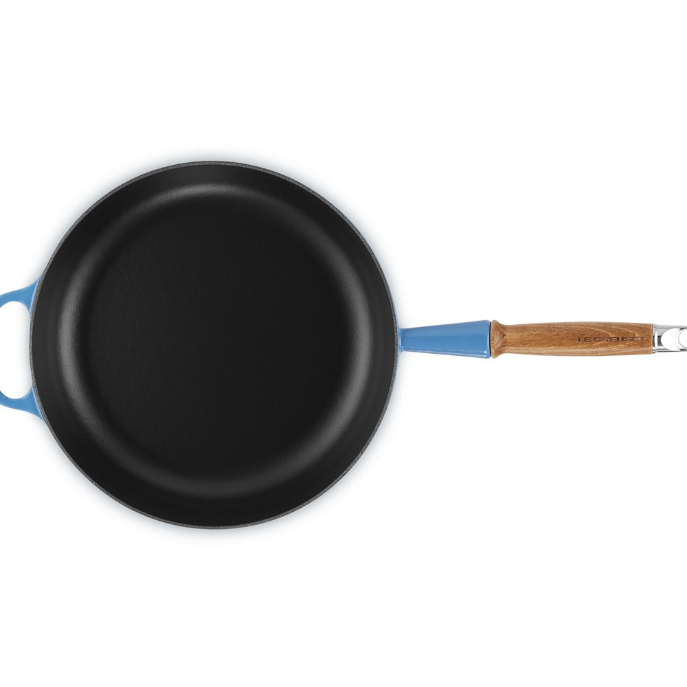 Padella rotonda con superficie nera opaca, manico blu chiaro e dettagli in legno, su sfondo bianco.