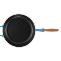 Padella rotonda con superficie nera opaca, manico blu chiaro e dettagli in legno, su sfondo bianco.