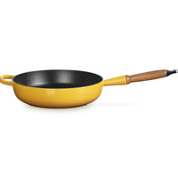 Padella gialla con manico in legno, superficie interna nera e fondo lucido, leggermente inclinata su sfondo bianco.