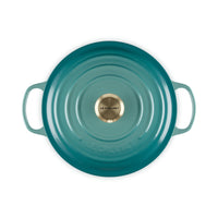 Casseruola ovale di colore turchese con manici, superficie liscia e centrale dorato con scritta "LE CREUSET".